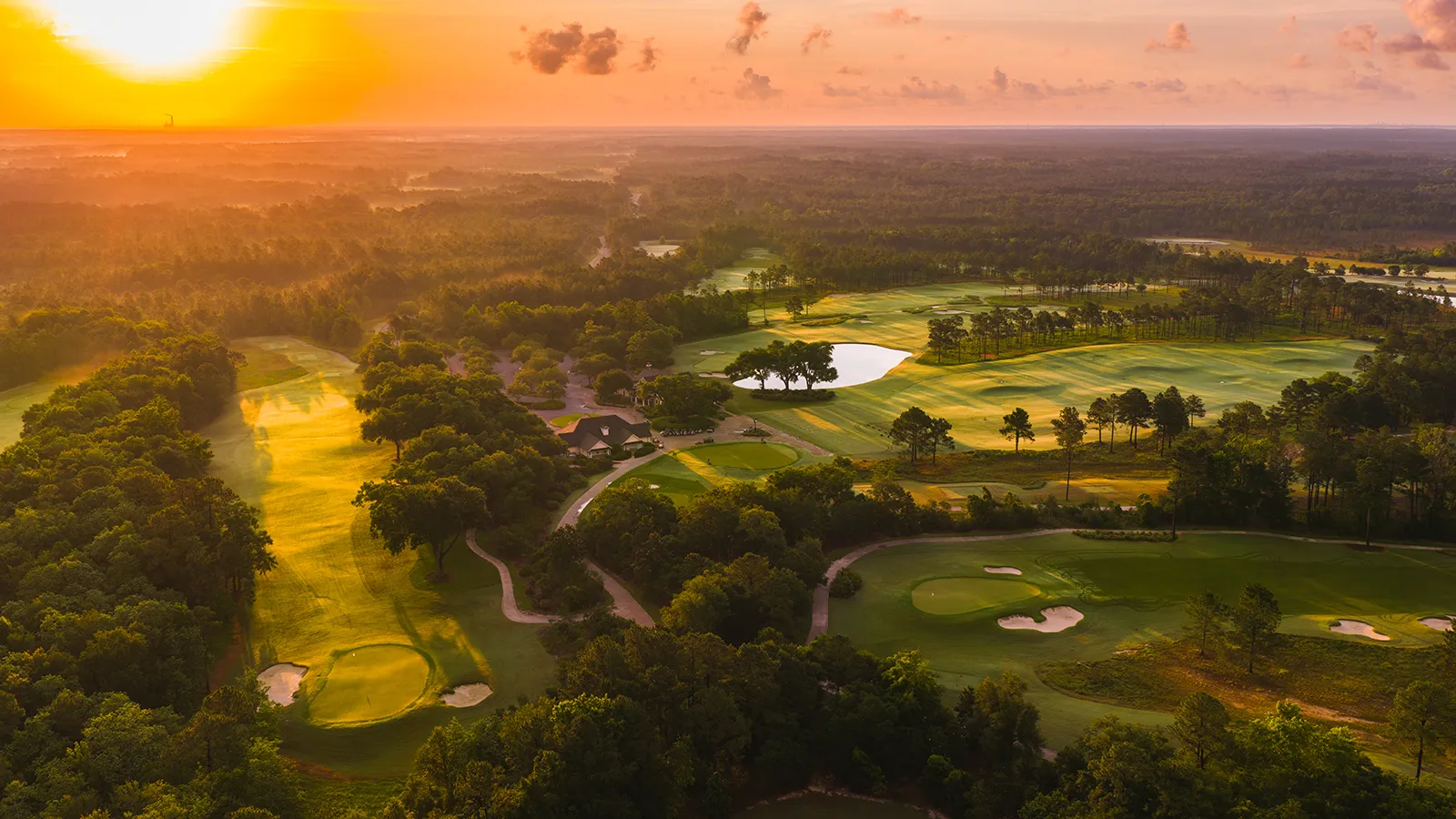 Aerial view of The Preserve Golf Club at sunrise, with fairways, bunkers and water winding through pine woods