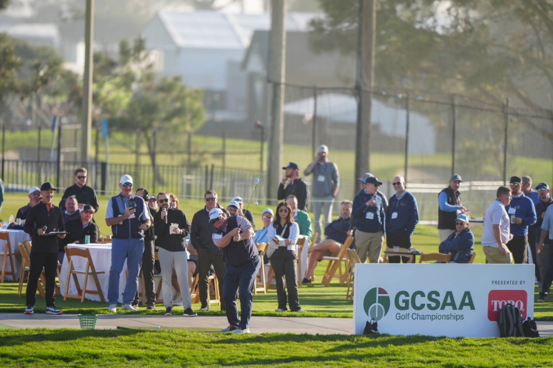 Players and spectators gathered around a tee at the Toro Par 3 Shootout, with a GCSAA Golf Championships and Toro banner behind the tee box.
